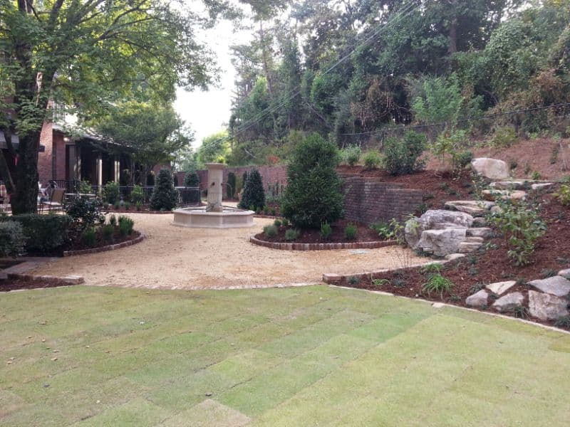 Lush landscaped backyard with stone pathways, decorative shrubs, and a central fountain, designed by John Russell Landscape Architect for an elegant outdoor living space.