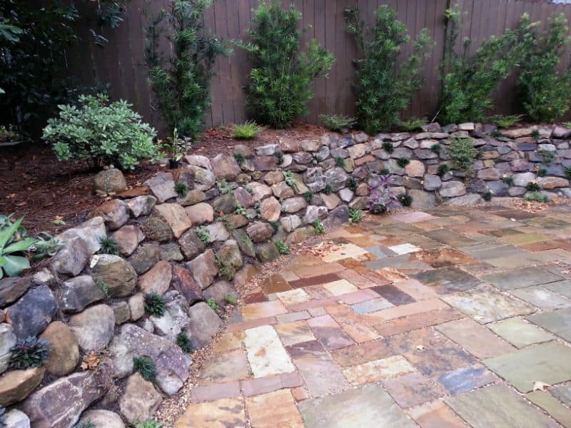 Natural stone retaining wall and stamped concrete patio design by John Russell Landscape Architect, showcasing landscape architecture, outdoor living space, and garden landscaping services.