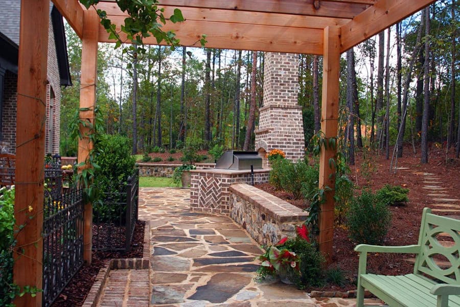 Modern outdoor living space with stone patio, built-in grill, and lush landscaping by John Russell Landscape Architect.