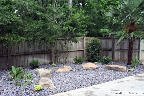 Large backyard landscape design with rocks and lush greenery, showcasing professional landscape architecture services by John Russell.