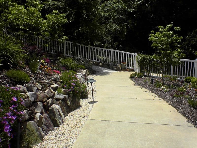Lush landscaped pathway with decorative rock edging and vibrant plants, designed by John Russell Landscape Architect, showcasing elegant garden and outdoor space design.