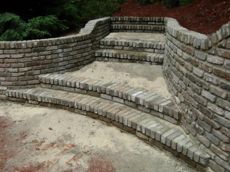Stone brick garden staircase with curved retaining wall, designed by John Russell Landscape Architect, showcasing outdoor landscaping and hardscape features.