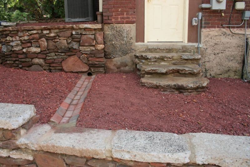 Red mulch landscaping with stone and brick accents in a residential yard, showcasing professional outdoor design by John Russell Landscape Architect.
