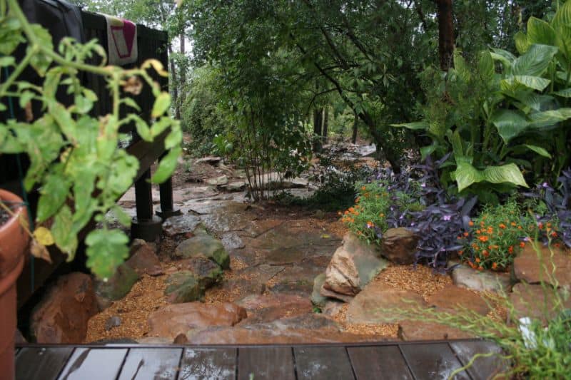 Rustic natural stone garden pathway with lush green plants and colorful flowers, landscaped by John Russell Landscape Architect for serene outdoor spaces.