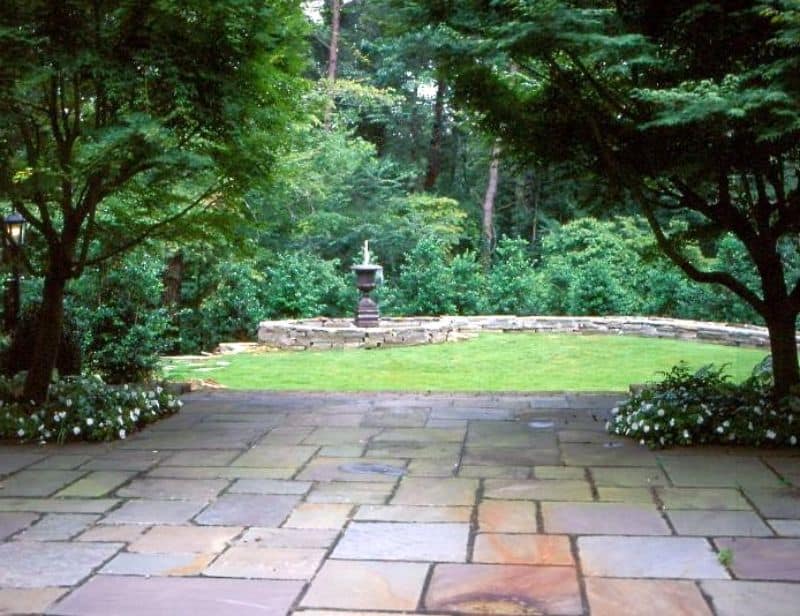 Natural stone patio with lush green landscaping and a decorative fountain, showcasing expert landscape design by John Russell Landscape Architect.