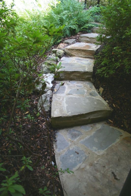 Natural stone garden pathway with irregular flagstone steps surrounded by lush greenery and plants.