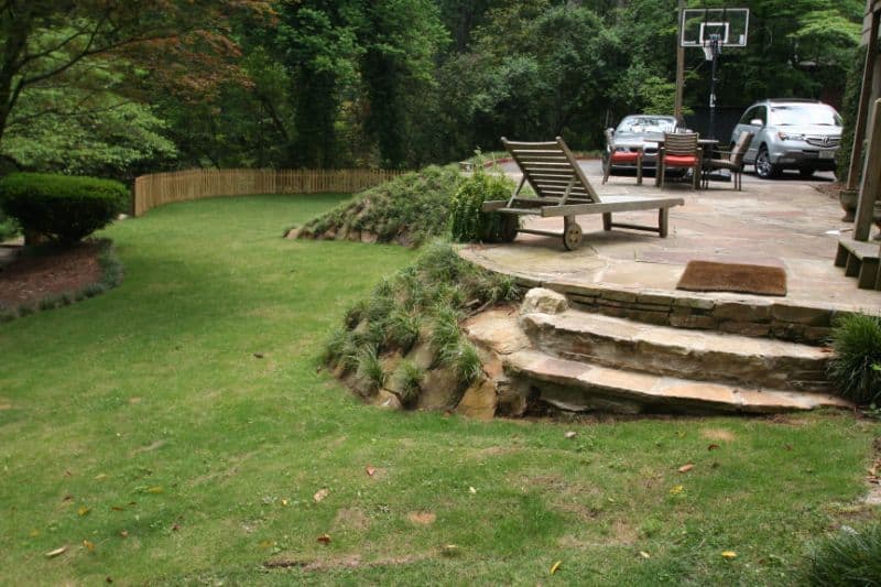 Lush backyard landscape with tiered stone steps, manicured lawn, outdoor seating, and a basketball hoop, designed by John Russell Landscape Architect for functional and aesthetic outdoor living.