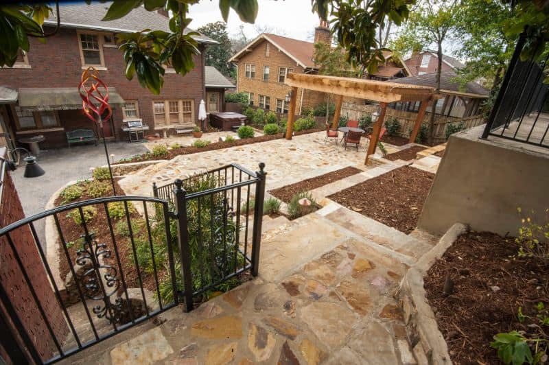 Natural stone patio landscape design with iron gate and outdoor seating area in residential backyard.