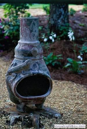 Vase garden sculpture with intricate patterns, surrounded by lush greenery and blooming flowers in a landscaped outdoor space.