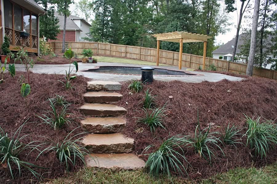 Natural stone staircase leading to a backyard patio with a hot tub and wooden pergola, designed by John Russell Landscape Architect. Beautiful landscape transformation with elegant plantings and fencing.