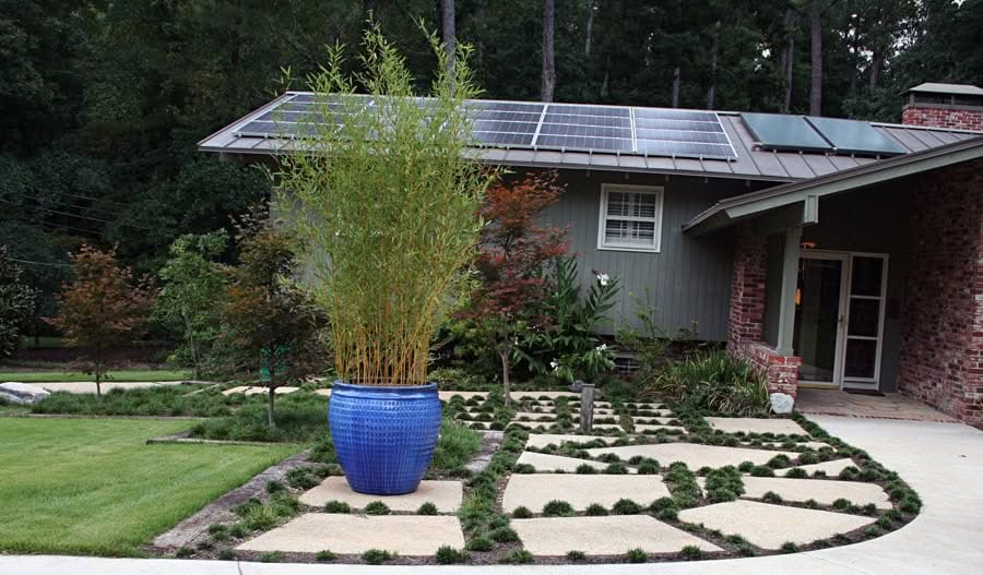 Modern landscape design with a custom garden featuring geometric paver patterns, lush greenery, and solar panels on the roof by John Russell Landscape Architect.