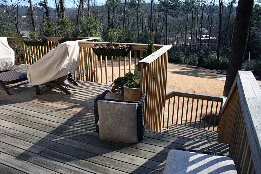 Patio deck with wooden railing and outdoor furniture, scenic wooded background, landscape design by John Russell Landscape Architect, residential outdoor space, natural setting, hardwood flooring, relaxing patio area.