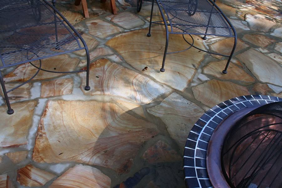 Natural stone patio with wrought iron chairs for outdoor living, designed by John Russell Landscape Architect, showcasing exquisite hardscape craftsmanship and landscape design expertise.