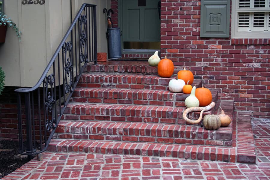 Pumpkin decorations on brick front steps of a house, Halloween autumn outdoor decor, cozy fall exterior design by landscape architect.