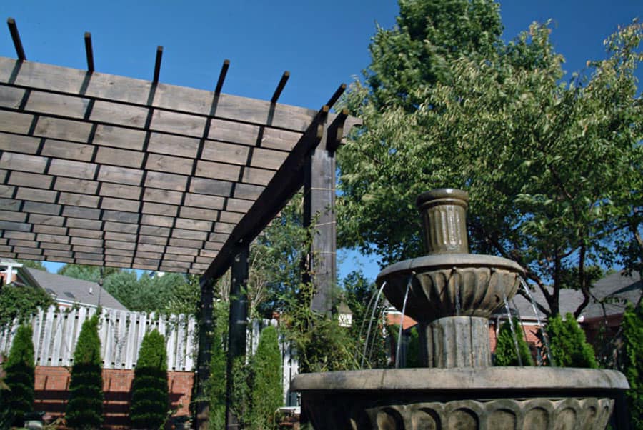 Modern outdoor water fountain with garden greenery and wooden pergola in a landscaped backyard.