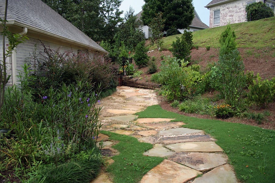 Stone pathway in landscaped garden with lush greenery and flowering plants, designed by John Russell Landscape Architect in a residential backyard setting.