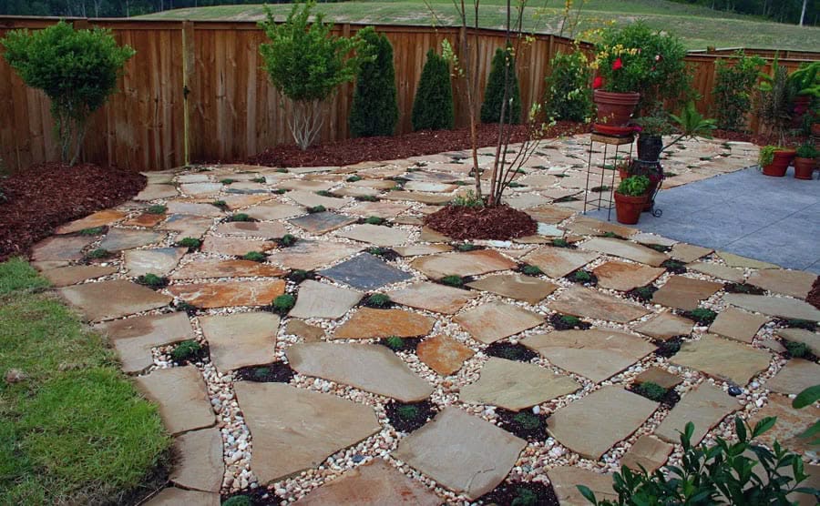 Natural flagstone patio with colorful stones, lush greenery, and decorative potted plants in a backyard garden setting.