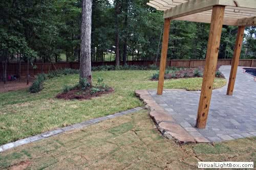 Lush backyard landscape design with a wooden pergola, stone patio, and manicured lawn showcasing professional landscape architecture services.
