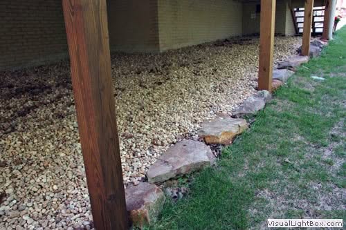 Natural stone landscape edging with gravel and wooden supports in a backyard garden.