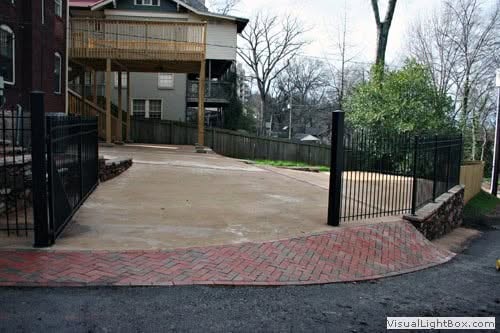 Natural stone and brick driveway with black metal fencing and wooden deck in residential landscape design by John Russell Landscape Architect.