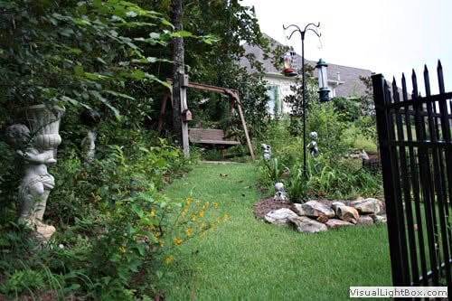 Lush backyard garden landscape design featuring a wooden bench, decorative statues, and vibrant flowers, crafted by John Russell Landscape Architect.