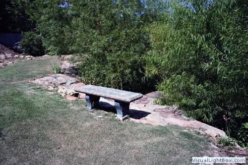 Rustic stone bench in lush garden landscape by John Russell Landscape Architect, blending natural materials with outdoor greenery for tranquil aesthetic design.