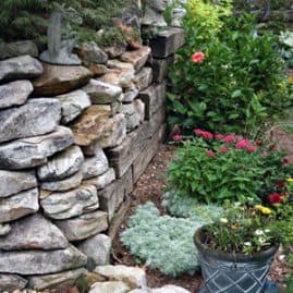 Lush garden with stone retaining wall, decorative sculptures, colorful flowers, and lush greenery showcasing expert landscape design by John Russell Landscape Architect.