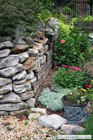 Lush garden with stone retaining wall, decorative sculptures, colorful flowers, and lush greenery showcasing expert landscape design by John Russell Landscape Architect.