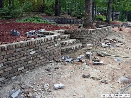 Exquisite brick retaining wall and stairway under construction in a lush, wooded landscape by John Russell Landscape Architect.