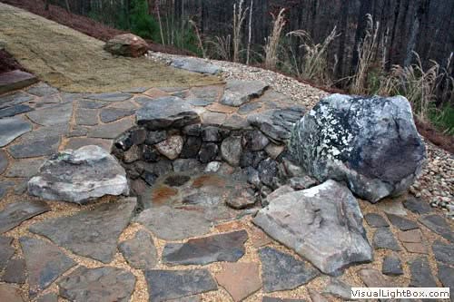 Rugged stone fire pit with large rocks and flagstone patio, ideal for outdoor gatherings and landscape design by John Russell Landscape Architect.