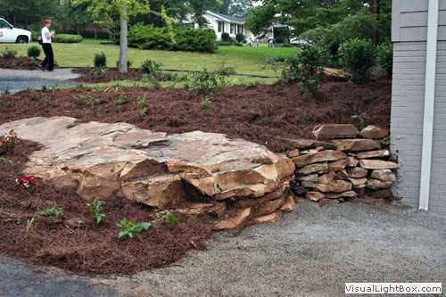 Natural stone retaining wall in a landscaped yard, designed by John Russell Landscape Architect, showcasing expert landscape design and durable rockwork.