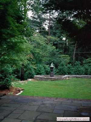 Lush landscape garden with fountain, mature trees, and manicured lawn, designed by John Russell Landscape Architect, blending natural beauty with functional outdoor space.