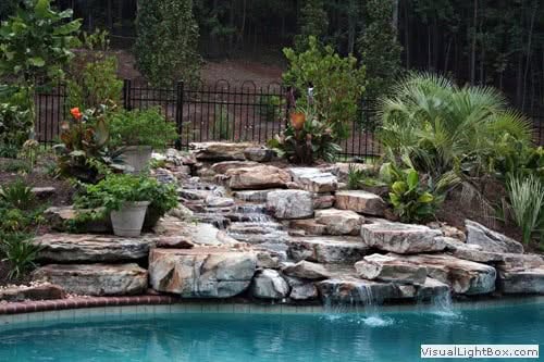 Lush backyard landscape featuring a natural stone waterfall, tropical plants, and a serene swimming pool designed by John Russell Landscape Architect for tranquil outdoor living.