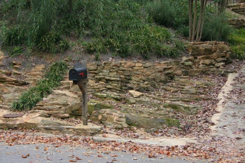 Stone retaining wall with lush greenery by John Russell Landscape Architect, showcasing expert landscape design and craftsmanship for residential outdoor spaces.