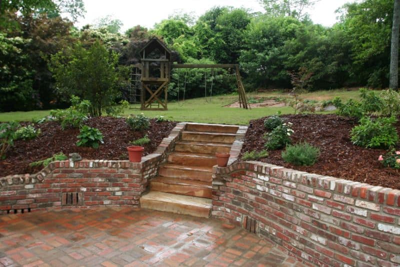 Handcrafted brick patio with stone steps and landscaped garden featuring lush greenery and mature trees.
