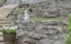 Natural stone retaining wall with decorative garden sculptures and potted plants, designed by John Russell Landscape Architect. Beautiful landscape architecture showcasing outdoor space transformation.