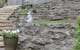 Natural stone retaining wall with decorative garden sculptures and potted plants, designed by John Russell Landscape Architect. Beautiful landscape architecture showcasing outdoor space transformation.